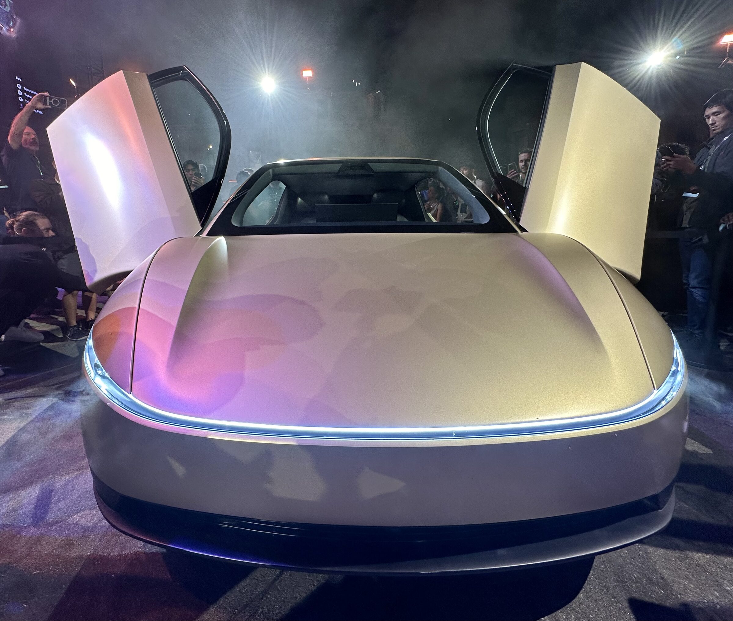 Front of a Tesla Cybercab at night, doors raised, no steering wheel visible.