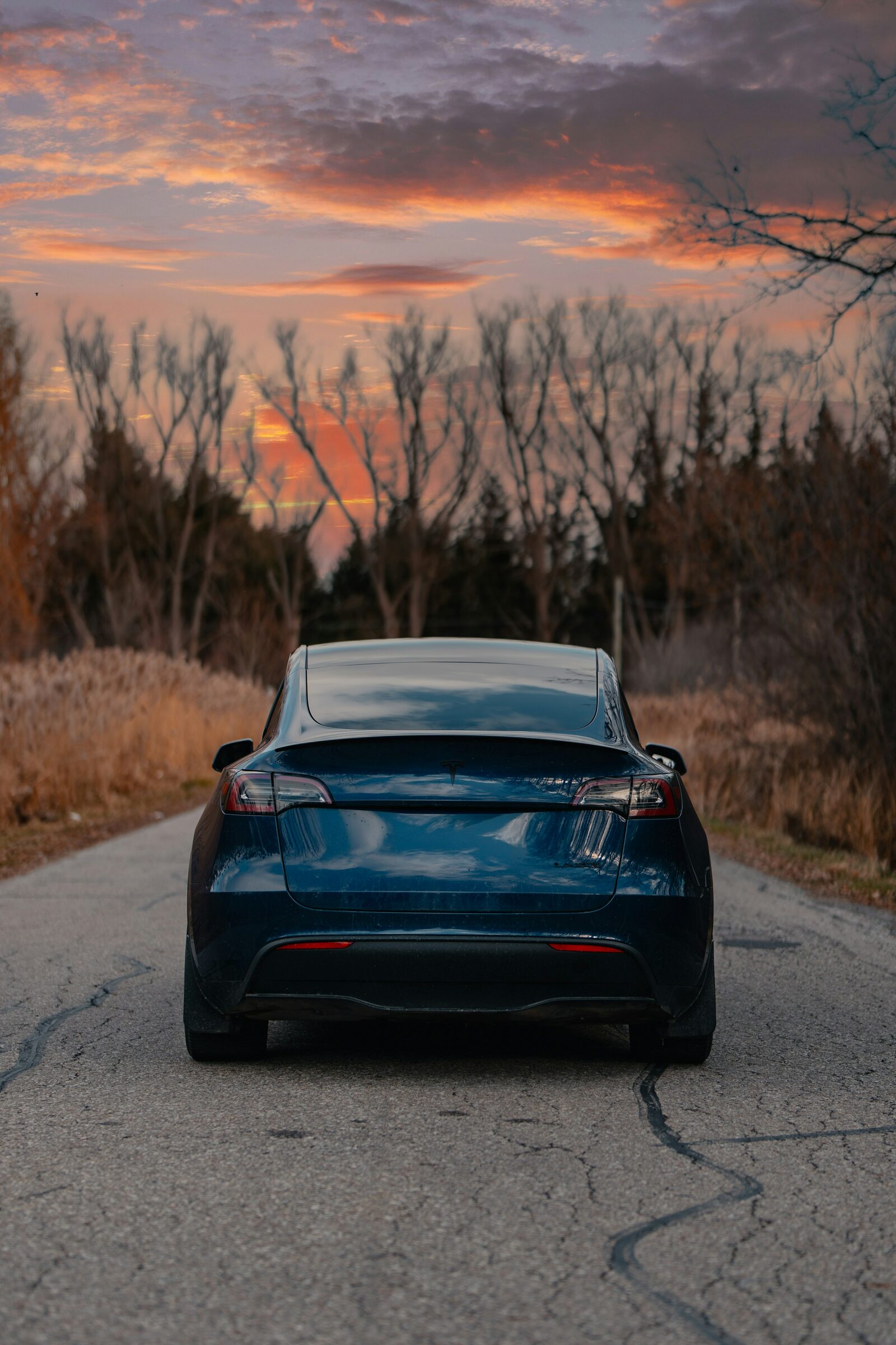 A blue Tesla Model Y at dusk on a quiet road.